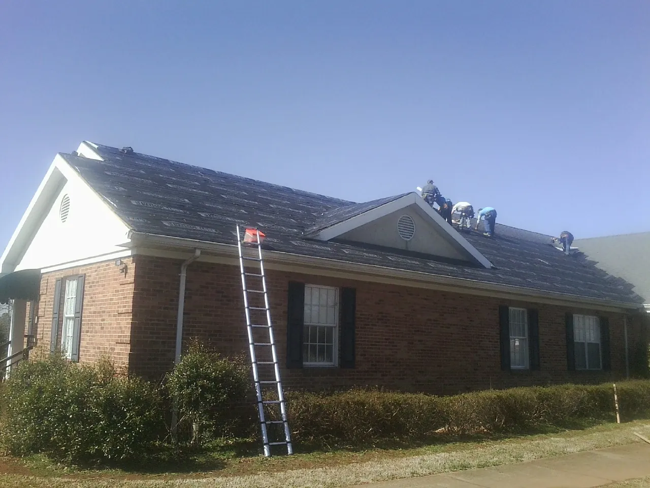 Crew tearing shingles off a brick ranch roof with a ladder set — Emergency Roof Repair work by our crew in Plainville