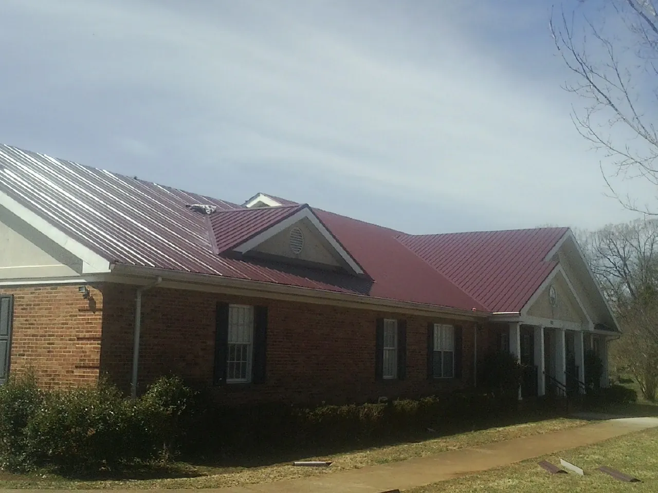 Red metal roof with gabled entries on a long brick building, from a Hail Damage Roof Repair job in Plainville