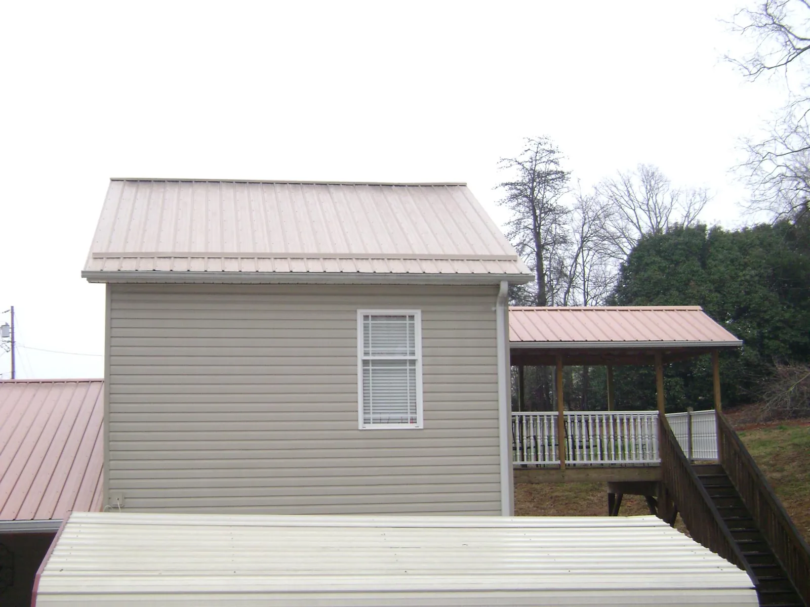Tan metal roofs on a two story addition and attached porch, from a Roof Replacement job in Plainville